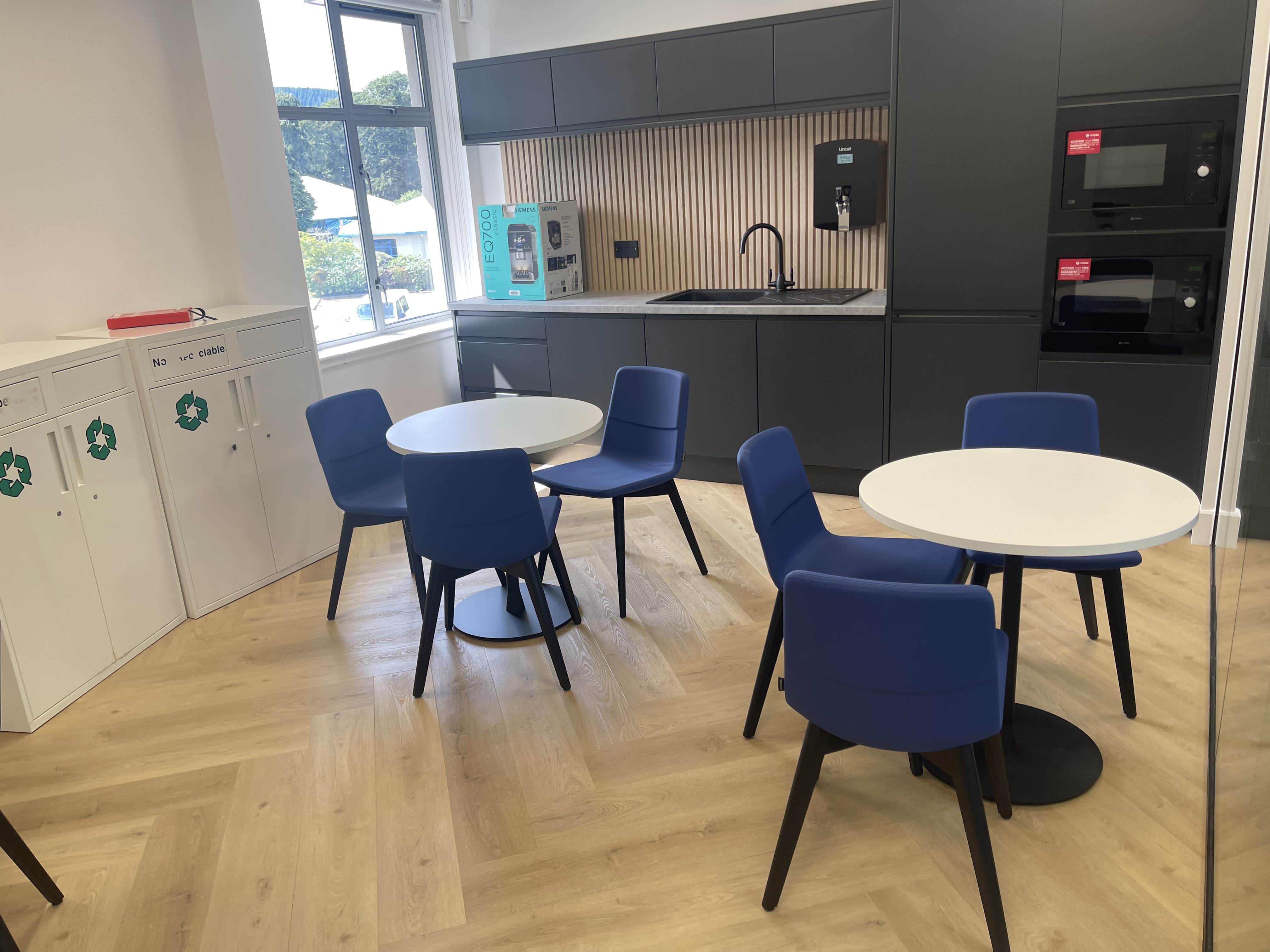 Clean office breakout area with tables and kitchen facilities