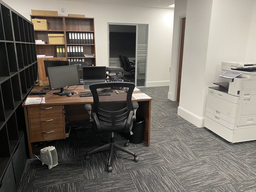 Office workspace with a desk, computer screens, printer and carpet tiles