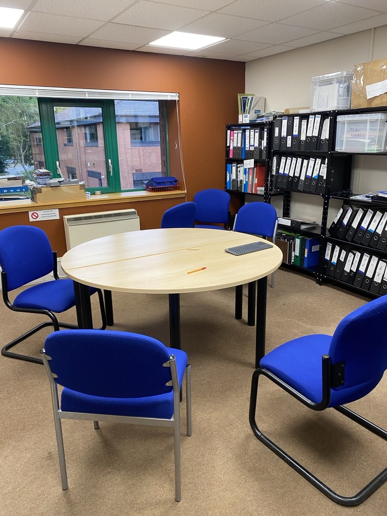 Office meeting area with a round table, blue chairs and filing shelves