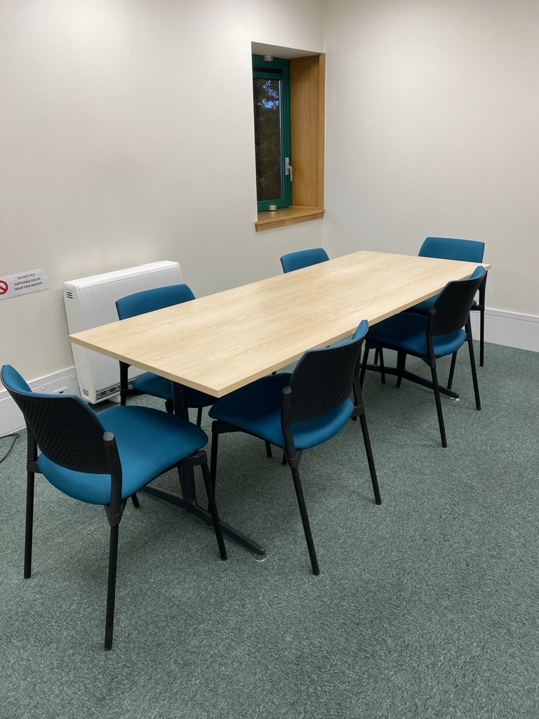 Small office meeting room with a wooden table and teal chairs
